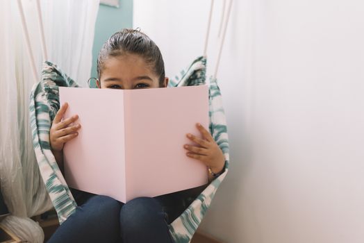 sweet happy little girl reading a book in her room near the window, funny lovely child having fun in kids room, copy space for text