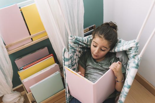 little girl surprised and excited reading a book at home near the window, funny lovely child having fun in her kids room, copy space for text