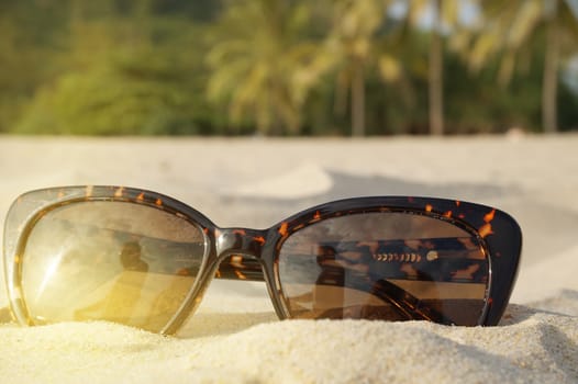 The concept of beach holidays and travel. Brown sunglasses on the sand on the beach, sunlight, place for text.