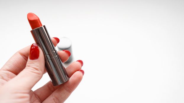 Woman Hand With Red Nails Holding Red Lipstick. Close Up Of Female Hand On White Background