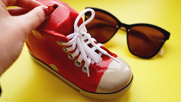 Moneybox in the form of sneakers. Sunglasses on a yellow background. The concept of savings on vacation and summer holidays. Money save