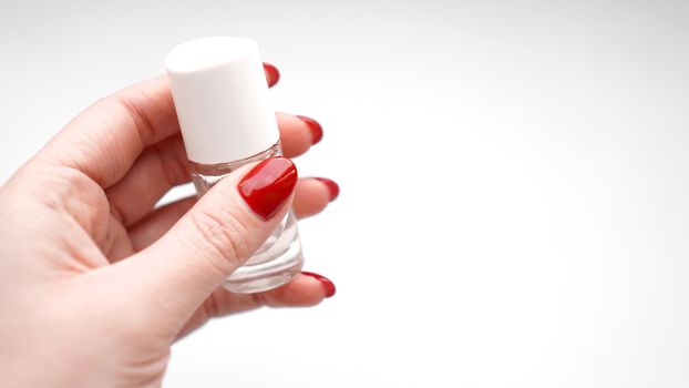 Girl with red nails holds clear polish or cuticle oil on white background. Health and nail care