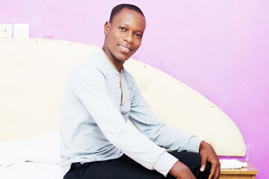 this young man dressed in the morning sitting on his bed cheerful face to the camera