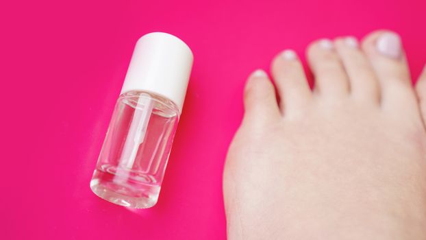 Pedicure with transparent nail polish on pink background. Healthy feet, health care