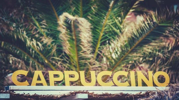 A Sign For Cappuccinos On A European Mediterranean Beach With Palm Trees