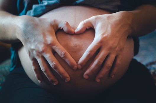 Pregnant woman with her hands and fingers making a heart on her belly, where her baby is.