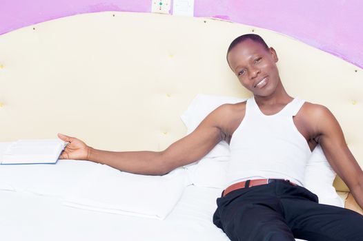 this young man is lying on his bed with a book in hand and trying to sleep .