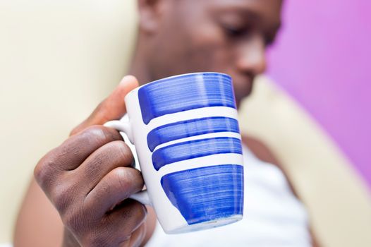 this man sitting against the wall holds in hand a cup of coffee