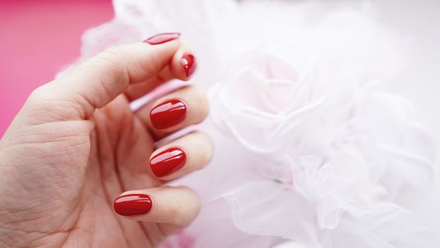 Beautiful female hand with red nails against the background of a white wedding bouquet