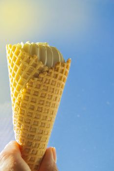 Summer, party, hand holding a vanilla ice cream cone against the blue sky and sunlight.