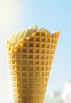 Vanilla ice cream cone against blue sky and sunlight.