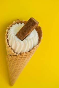 Vanilla ice cream in a waffle cone with chocolate on a yellow background, copy space.