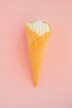 Vanilla ice cream in waffle cone on pink background, copy space, vertical shot.