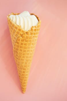 Vanilla ice cream in waffle cone on pink background, copy space, vertical shot.