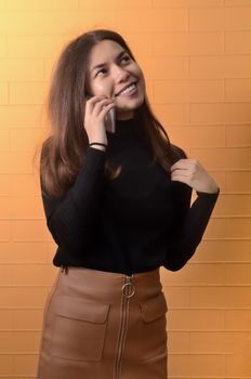 Portrait of a young Asian girl looks talking on the phone on a yellow brick background