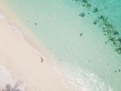 Aerial shot of woman looking up arms rised, enjoying the picture perfect white sand tropica beach on Mauritius island. Perfect tropical beach vacations concept.