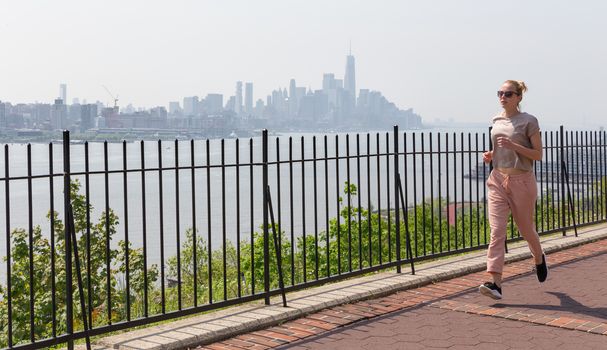 Healthy lifestyle. Woman is running on Hamilton ave by Hamilton park, New Jersey. Manhattan of New York City in the background.