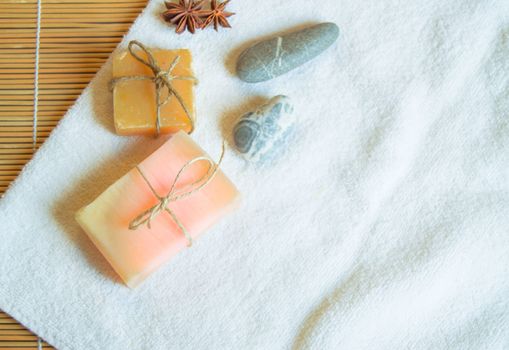 Spa setting with white towel, handmade soap, stones, on natural bamboo background, flat lay copy space.