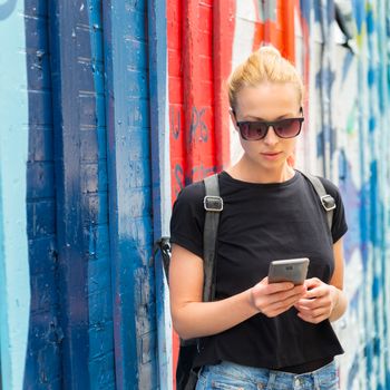 Closeup of female hipster with smart phone. Woman using smartphone against colorful graffiti wall in East Village, New York city, USA.