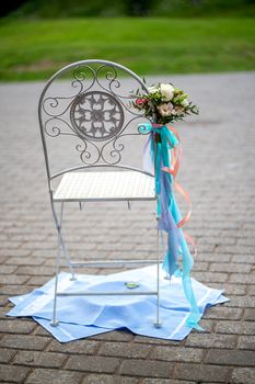 Chair decorated with bouquet of flowers and ribbons in wedding ceremony Wedding chair is placed on towels. 