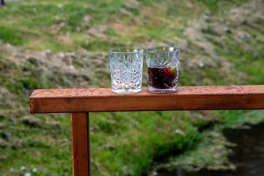 Two whiskey glasses on a wooden frame outdoors. Two glasses of  whiskey on green grass background.