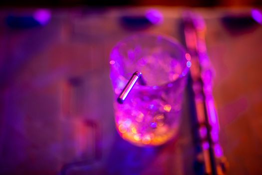 Closeup of abstract cocktail glass with straw on multicolor background. Glass of drink in multicolored light.