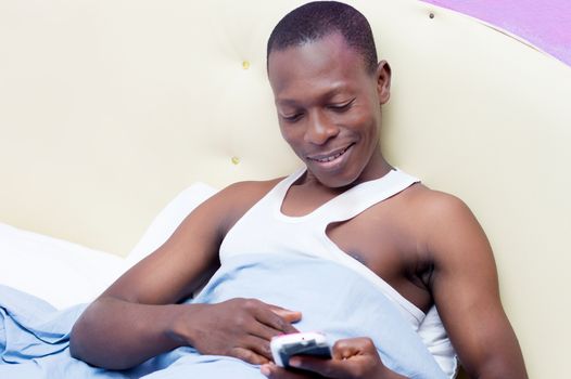 the young man lying in bed, consults his phone with smile after his call.