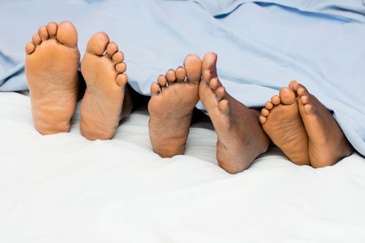 this family lying in bed show their bare feet and half covered