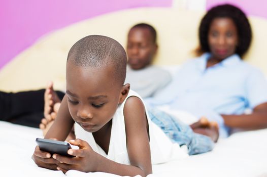 child plays with mobile phone of his parents who are watching in the background smiling .