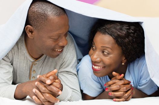 young couple lying under the cover looks, smiling.