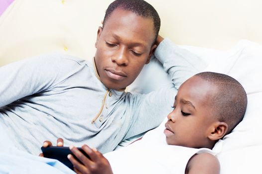 Dad looks at his child using mobile phone in bed