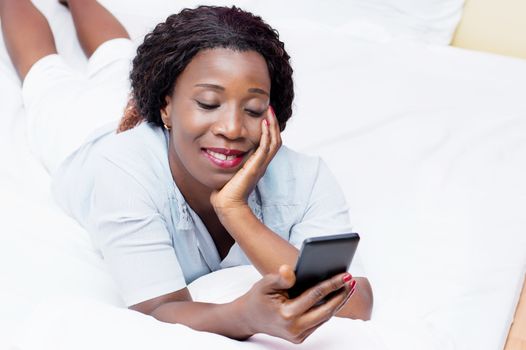 this smiling young woman lying on a bed sending a message on a mobile phone