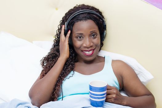 young woman lying in bed is pleased to wake up to music and a cup of coffee in hand