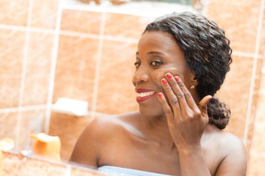 happy young woman applies cream on her face in the bathroom.