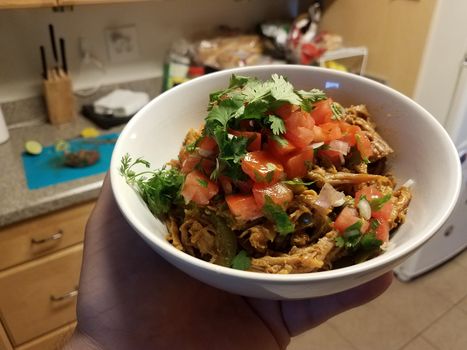 hand holding bowl of pulled pork and tomato and cilantro in kitchen