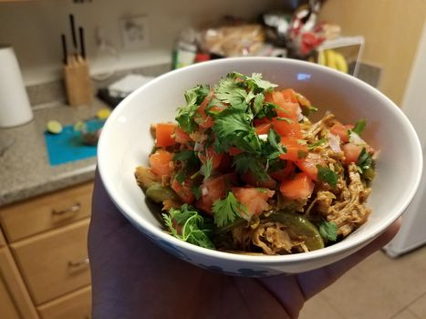 hand holding bowl of pulled pork and tomato and cilantro in kitchen