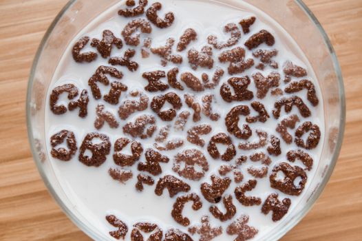 Top view of milk bowl, alphabet letters of cereal and chocolate flakes on wooden table, healthy Breakfast for kids and adults, diet and nutrition concept