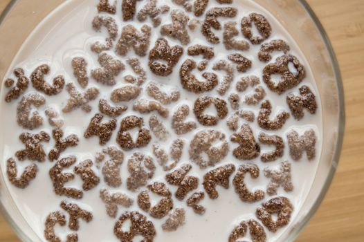 Top view of milk bowl, alphabet letters of cereal and chocolate flakes on wooden table, healthy Breakfast for kids and adults, diet and nutrition concept