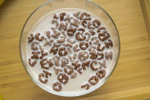 Top view of milk bowl, alphabet letters of cereal and chocolate flakes on wooden table, healthy Breakfast for kids and adults, diet and nutrition concept