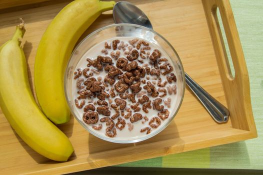 Bowl of oatmeal chocolate flakes in the shape of letters of the alphabet with milk on a wooden tray with bananas, healthy Breakfast concept for children and adults
