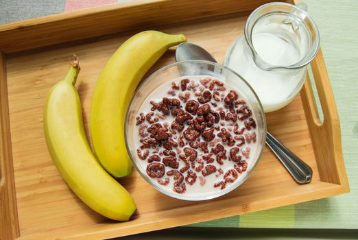 Bowl of oatmeal chocolate flakes in the shape of letters of the alphabet with milk on a wooden tray with bananas and a jug of milk, the concept of healthy healthy Breakfast for children and adults