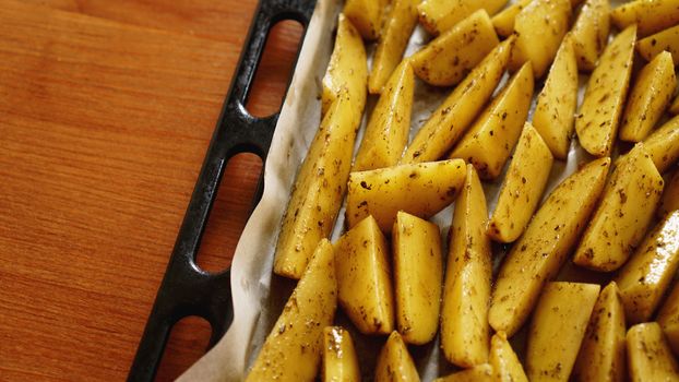 Sliced raw potatoes on a baking sheet with spices and rosemary, top view, copy space