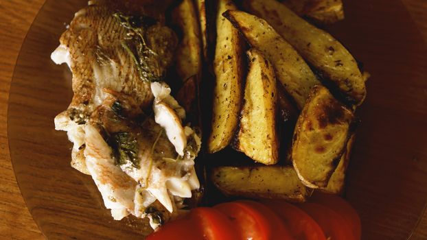 Fish dish - fried fish fillet with fried potatoes and vegetables with spices and rosemary, top view, copy space