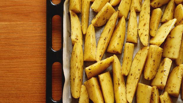 Sliced raw potatoes on a baking sheet with spices and rosemary, top view, copy space