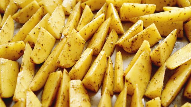 Sliced raw potatoes on a baking sheet with spices and rosemary, top view, copy space