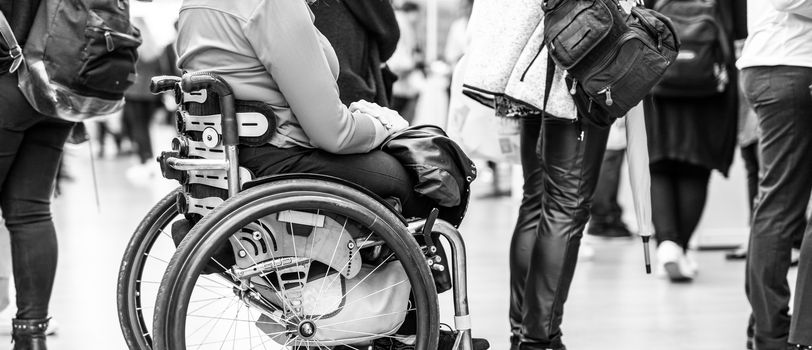Close up of unrecognizable hanicapped woman on a wheelchair waiting in line to perform everyday tasks.