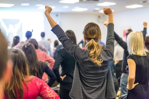 Life coaching symposium. Speaker giving interactive motivational speech at business workshop. Rear view of unrecognizable participants feeling empowered and motivated, hands raised high in air.