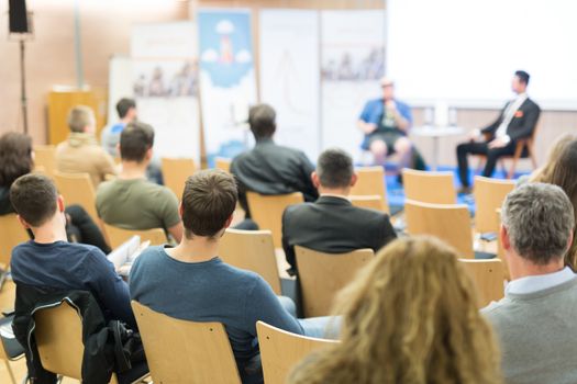 Round table discussion at business and entrepreneurship symposium. Audience in conference hall. Lens focus on unrecognized participant in rear of audience.