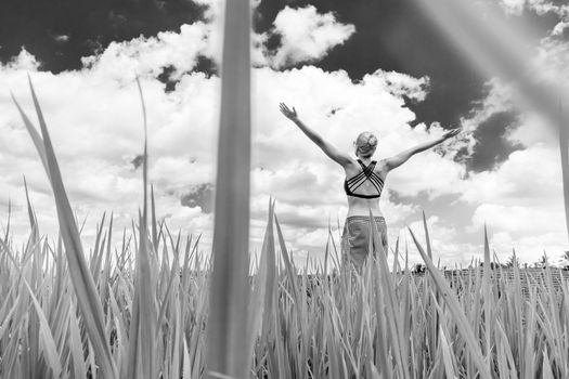 Relaxed healthy woman, arms rised, enjoying pure nature at beautiful green rice fields on Bali. Concept of healthy and clean environment, ecology, balance in life, freedom, happiness, and well being.