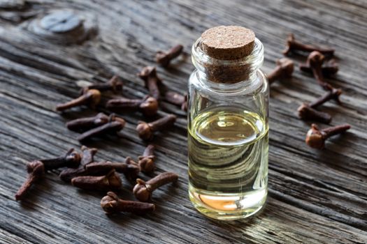 A bottle of clove essential oil on old wood with dried cloves in the background